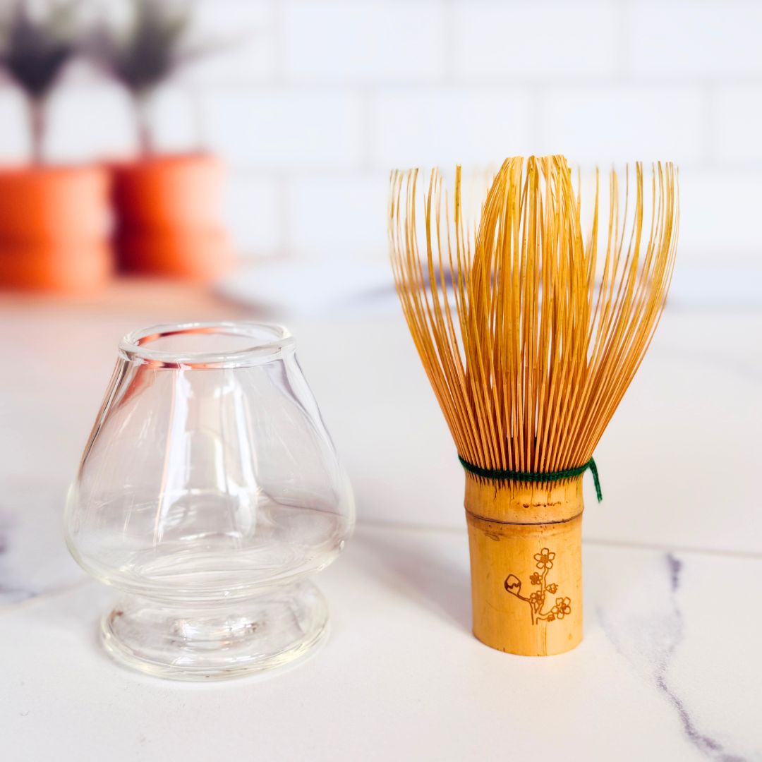 Bamboo whisk and clear glass container on a white surface