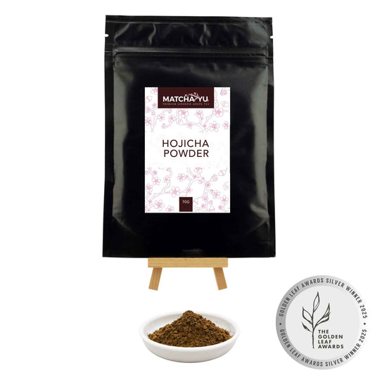 Black package of Matcha-yu Hojicha Powder with a small bowl of powder and an award badge on a white background