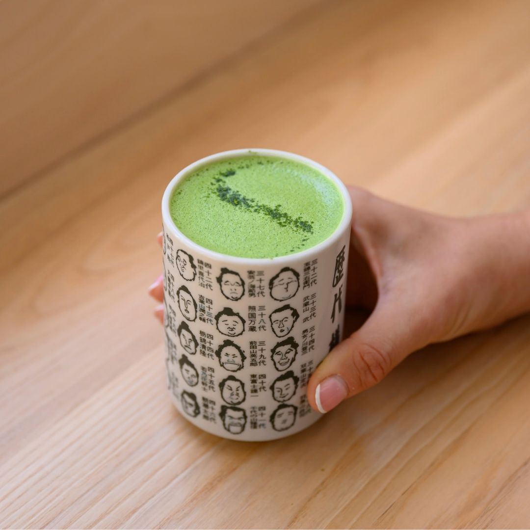 Hand holding a cup of green matcha tea with a wooden background