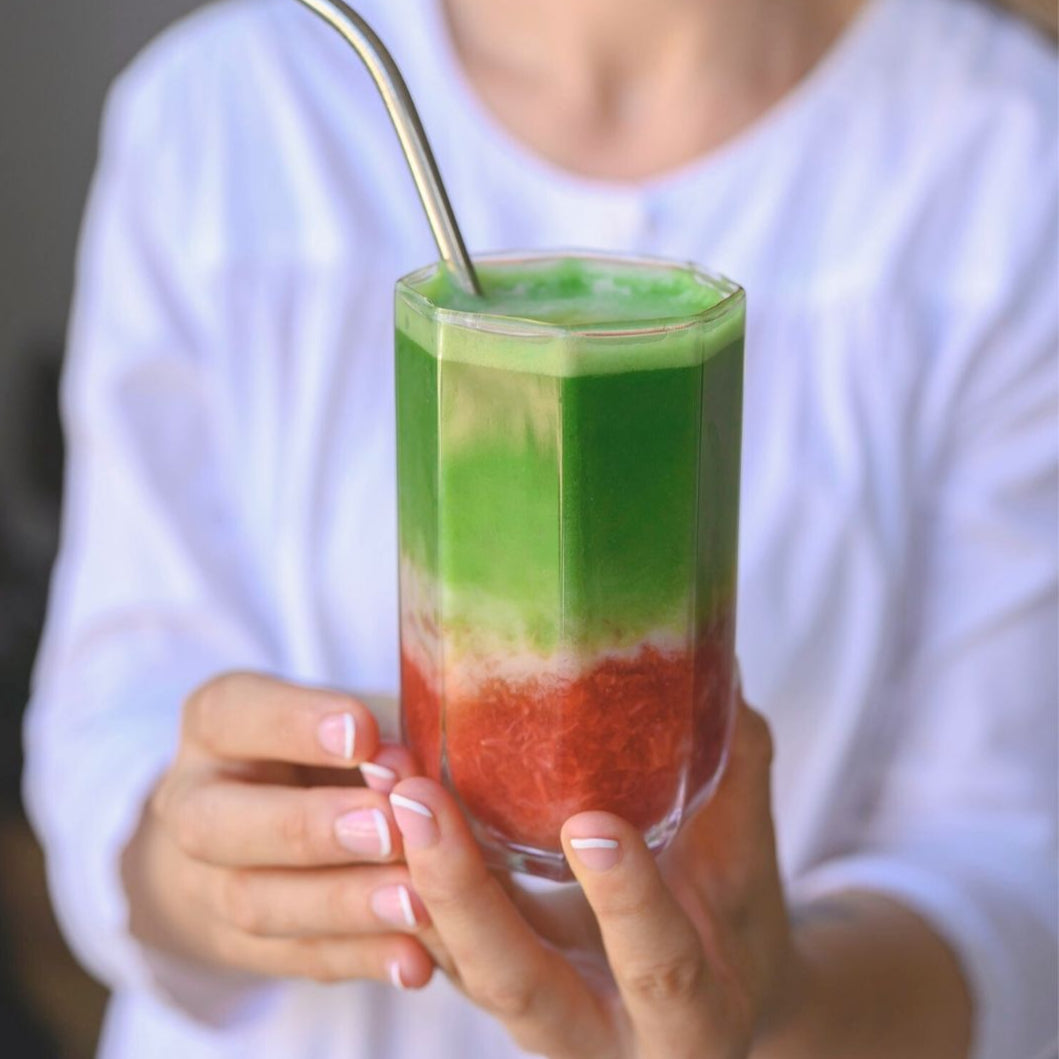 Person holding a glass of layered Iced Matcha and Strawberry with a straw.
