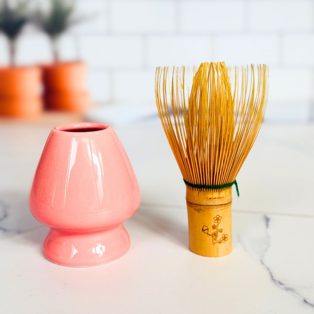 Pink ceramic whisk and wooden whisk on a white surface with blurred background