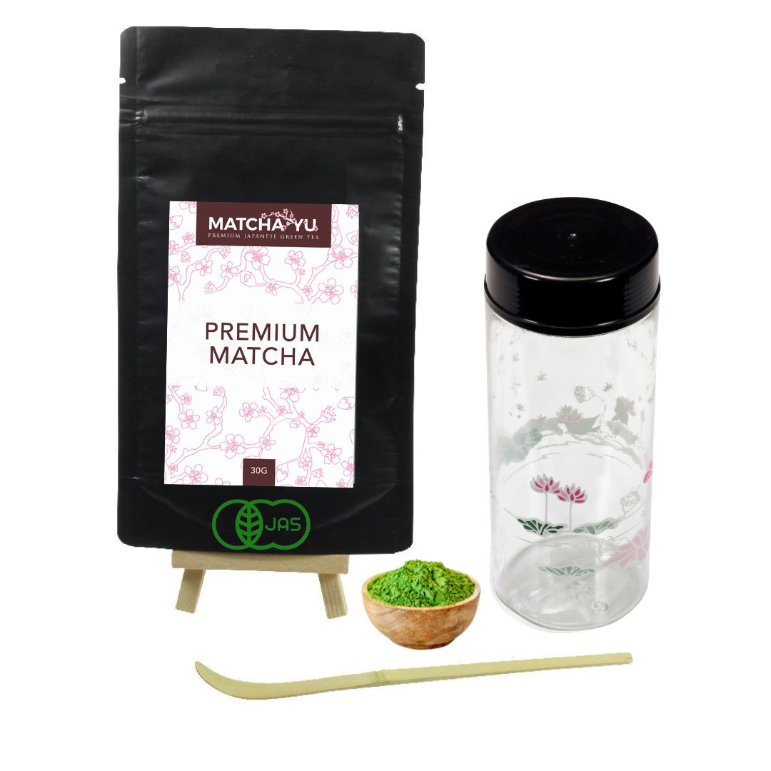 Matcha Yu premium matcha packaging with a small bowl of matcha powder, plastic shaker and scoop on a white background.