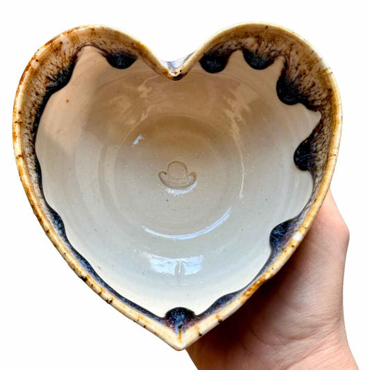 Heart-shaped ceramic bowl with a hand holding it against a white background