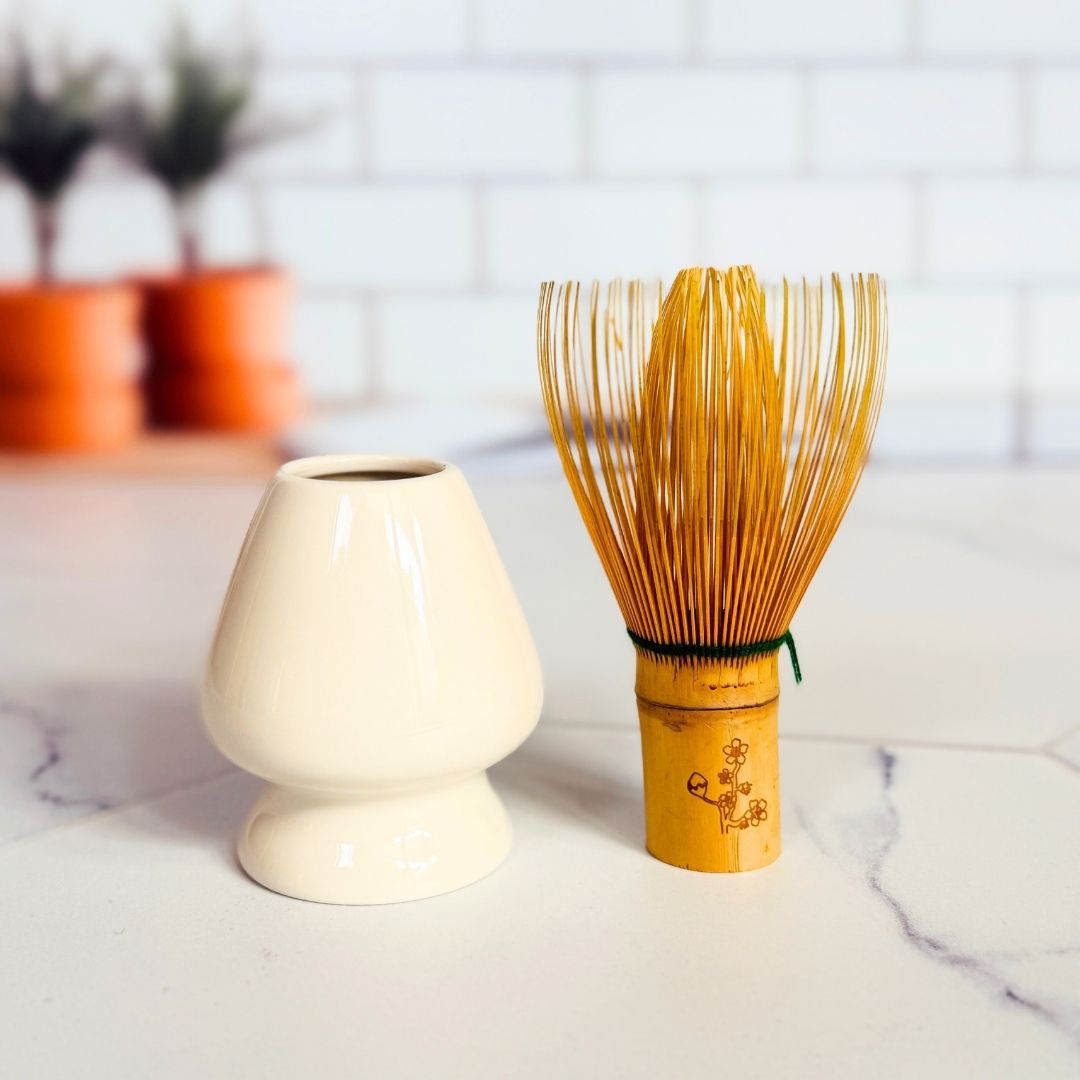 White ceramic whisk holder and wooden whisk on a marble surface with a blurred background