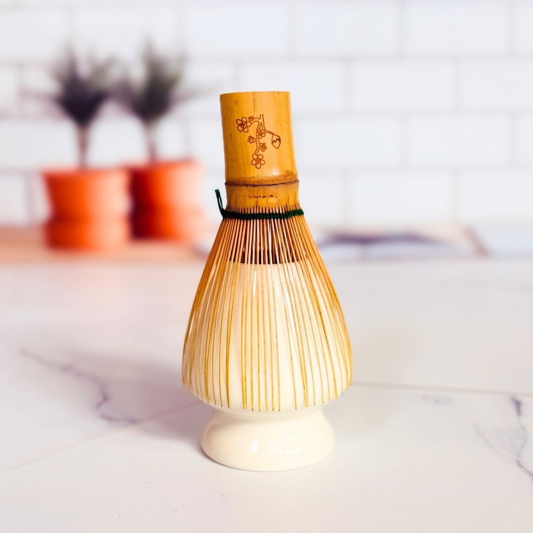 Bamboo whisk with wooden handle on a white surface with blurred background