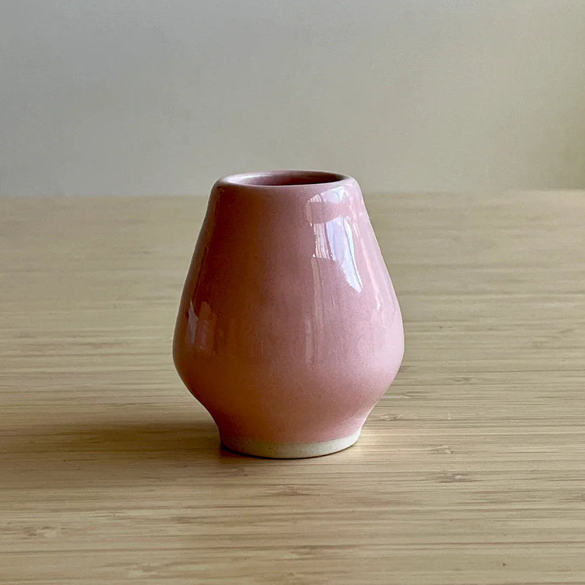 Pink ceramic whisk stand on a wooden surface with a plain background
