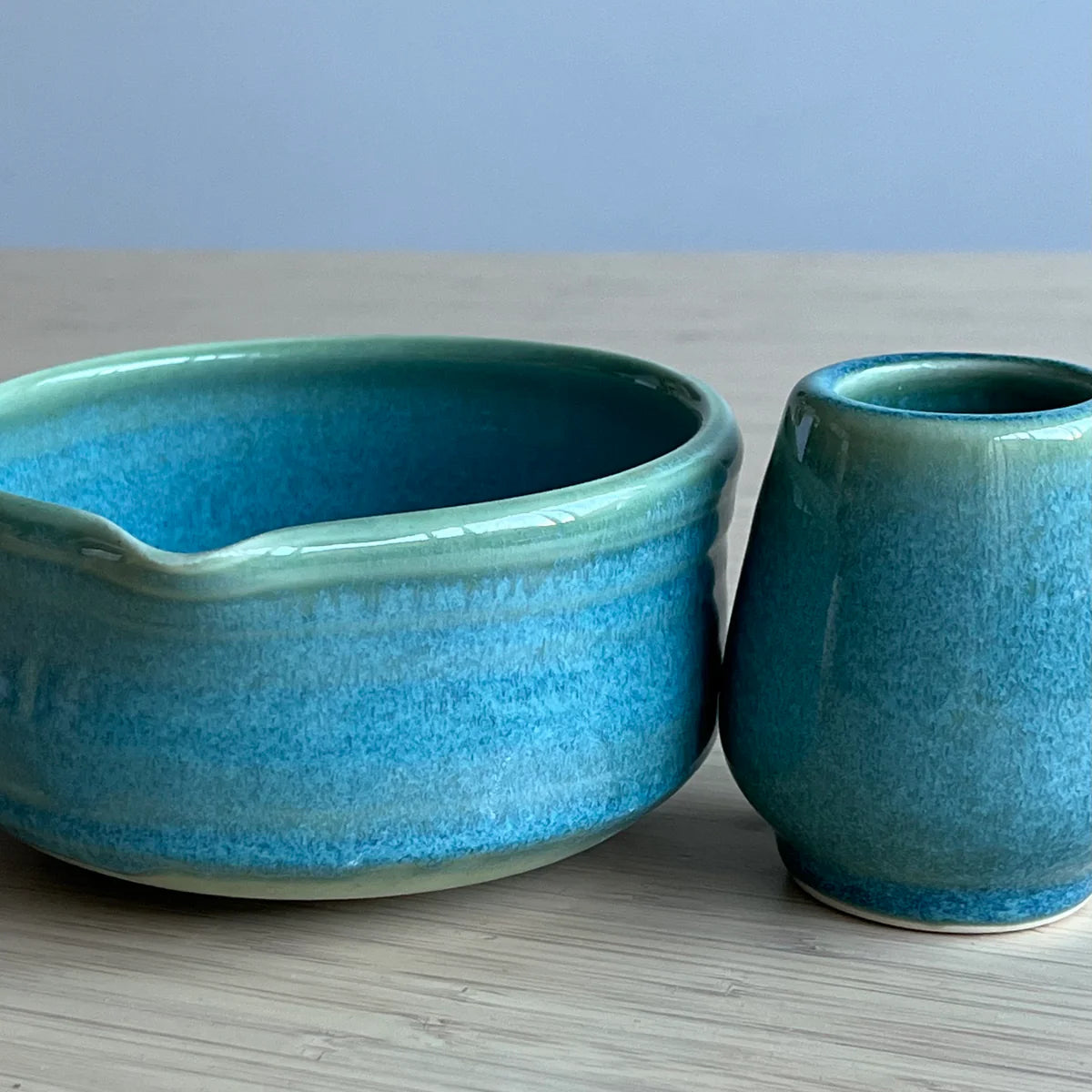 Two Green ceramic bowls on a light gray surface with a light blue background