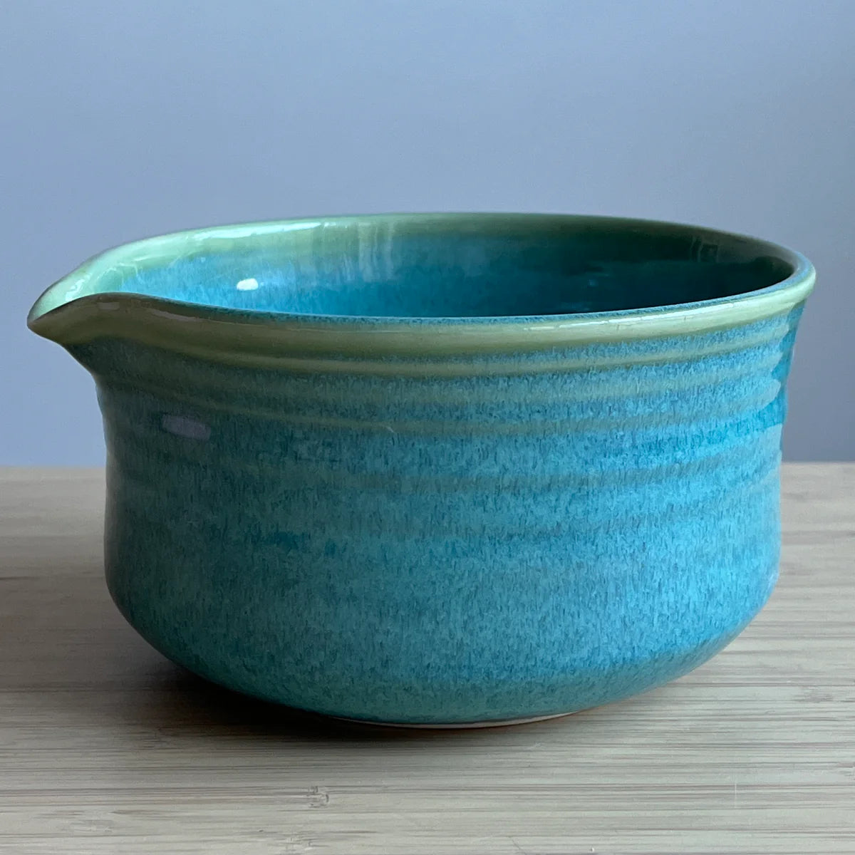 Turquoise green Matcha bowl on a wooden surface with a light blue background