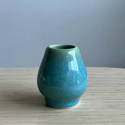 Green ceramic whisk stand on a wooden surface with a gray background