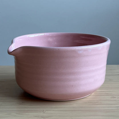 Pink ceramic Matcha bowl on a wooden surface with a gray background