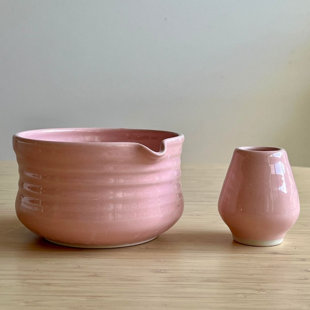 Pink Ceramic Matcha Bowl and whisk stand, on a wooden surface with a neutral background.