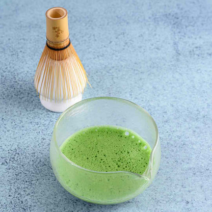Bowl of green matcha tea with a bamboo whisk on a light blue textured surface