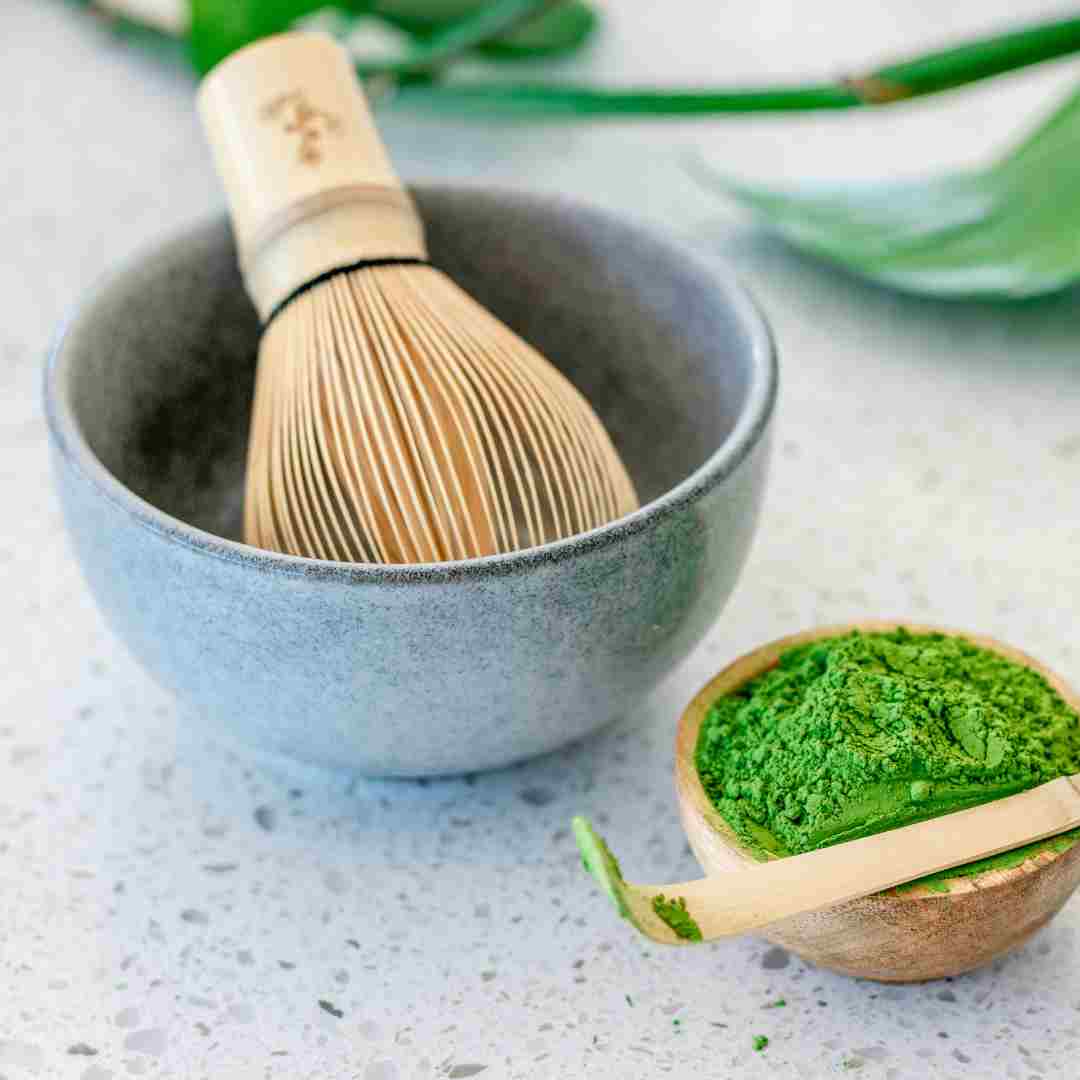 Matcha green tea bowl with wooden whisk and scoop on a light surface