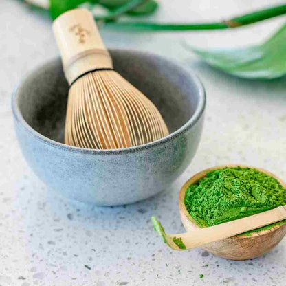 Matcha green tea bowl with wooden whisk and scoop on a light surface