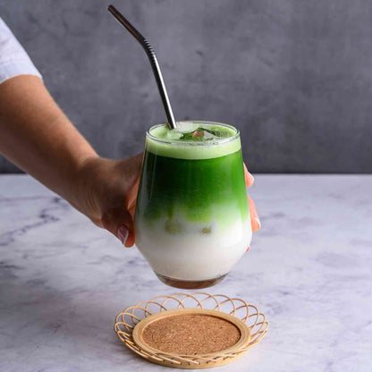 Hand holding a glass of layered green and white drink with a straw on a marble surface.