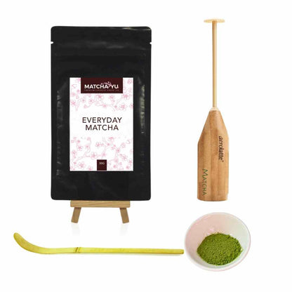 Matcha packaging, whisk, scoop, and bowl with matcha powder on a white background