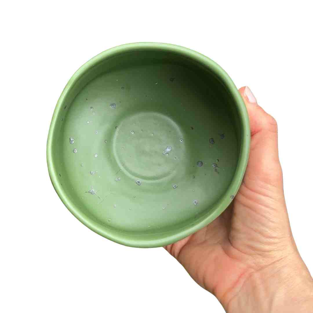Hand holding a green ceramic bowl against a white background