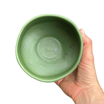 Hand holding a green ceramic bowl against a white background