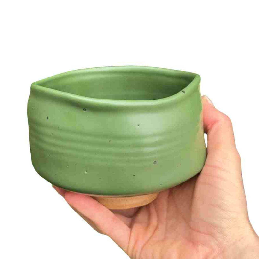 Hand holding a green ceramic pot against a white background