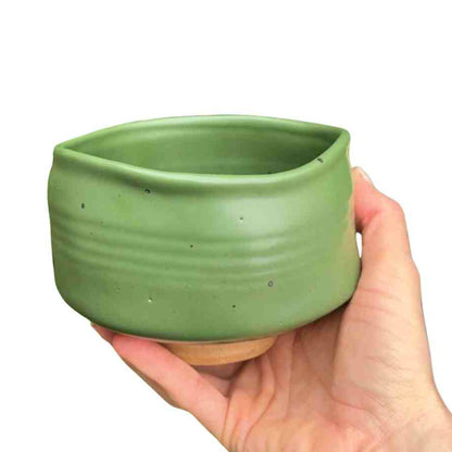 Hand holding a green ceramic pot against a white background