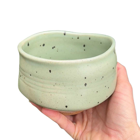 Hand holding a light green ceramic bowl with speckled pattern on a white background