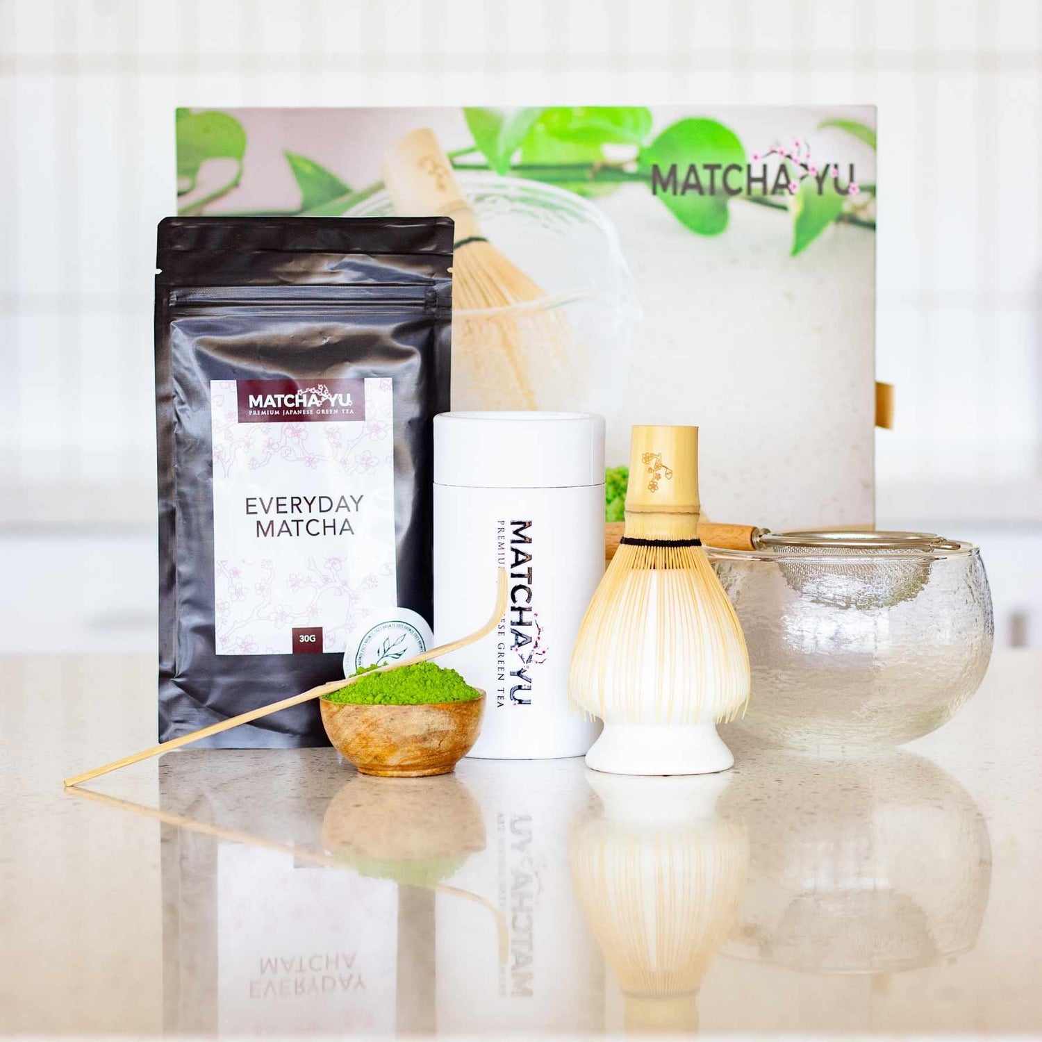 Matcha Yu tea products including a package, container, whisk, and bowl on a light surface.