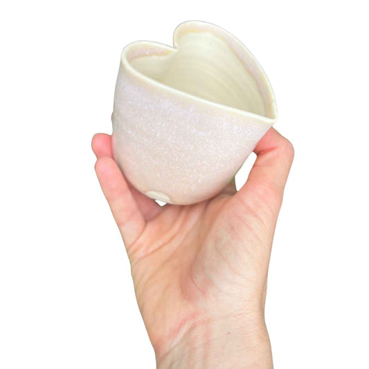 Hand holding a white ceramic heart-shaped cup against a white background