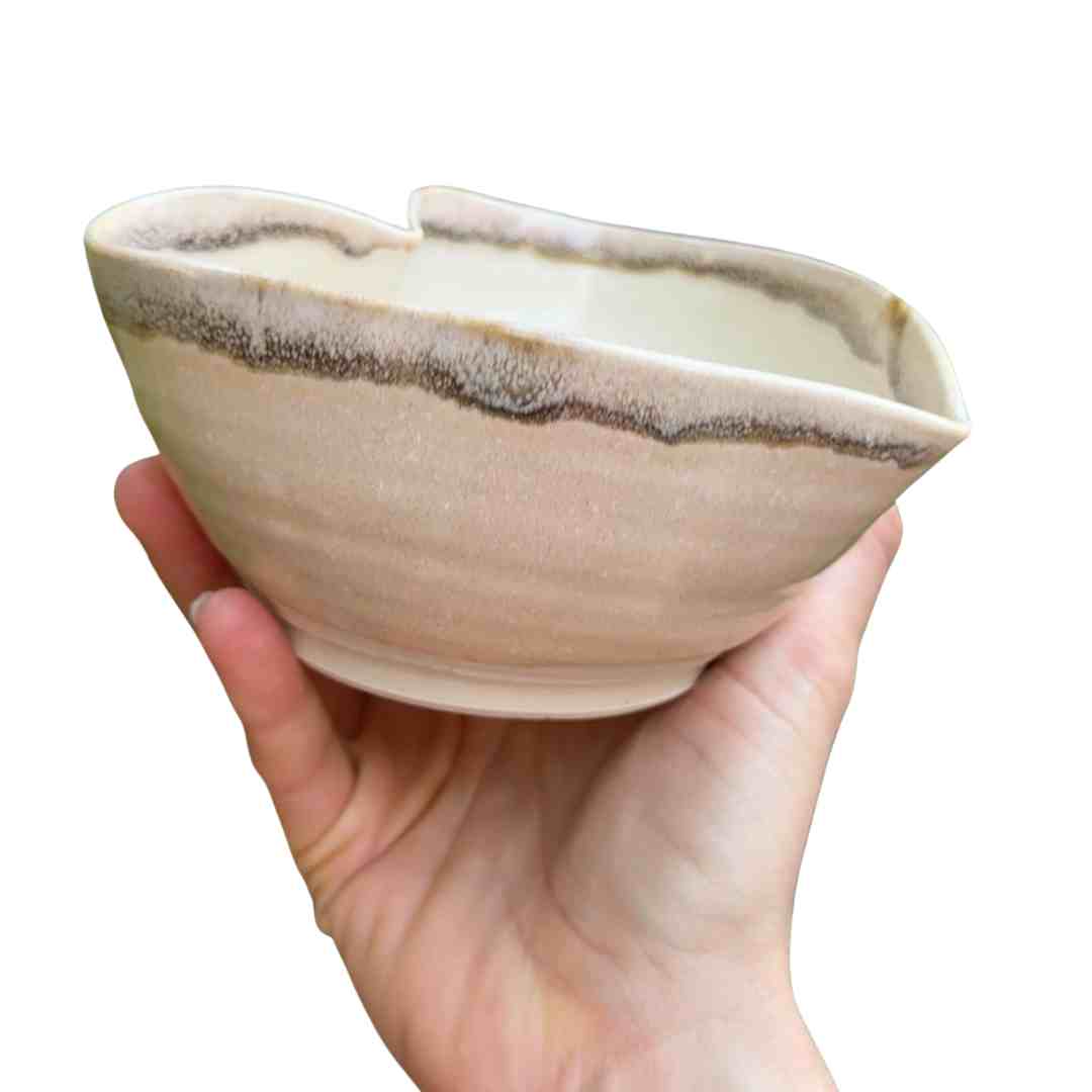 Hand holding a ceramic bowl with a white and brown design on a white background