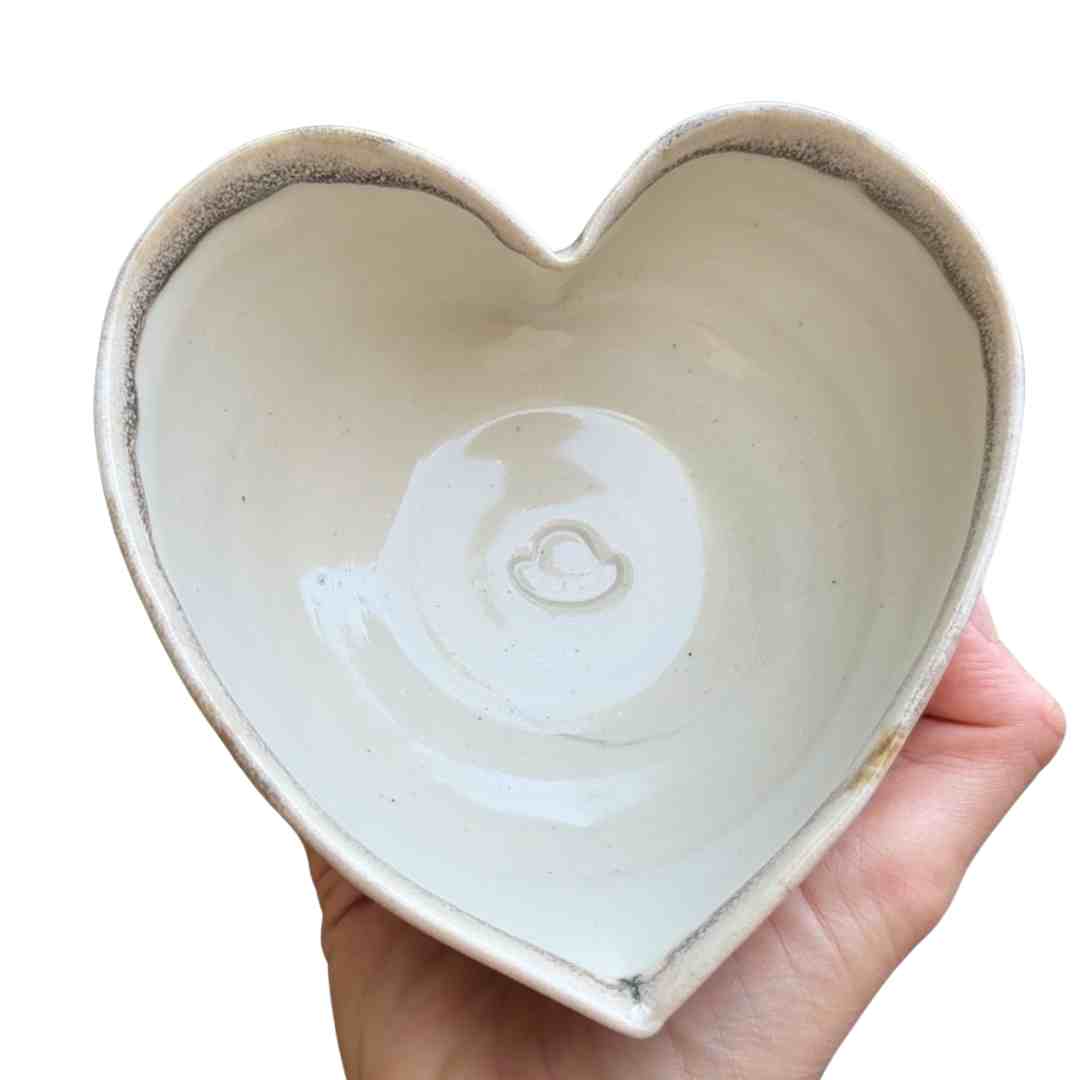 Heart-shaped ceramic dish held in a hand with a white background
