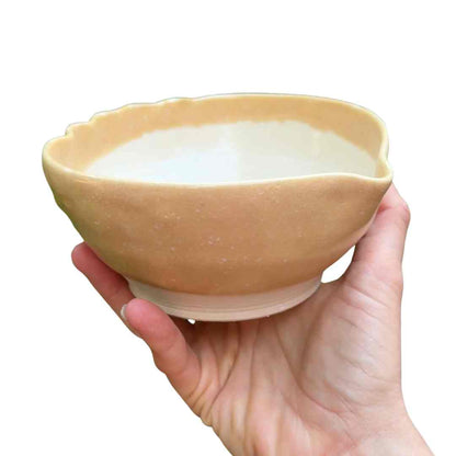 Hand holding a small ceramic bowl with a textured surface filled with a white substance on a white background