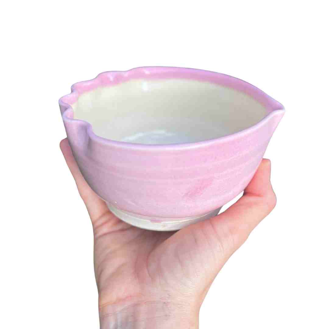 Hand holding a pink ceramic bowl with a white interior on a white background