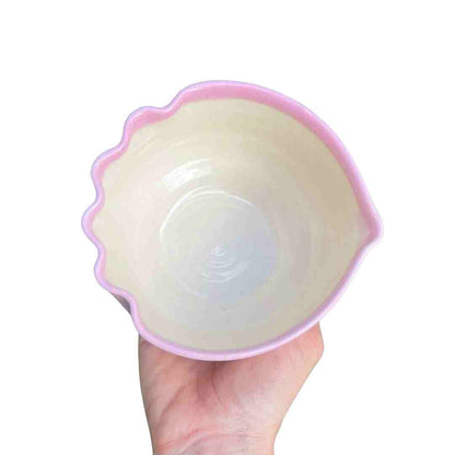 Shell-shaped container with pink rim held in a hand on a white background