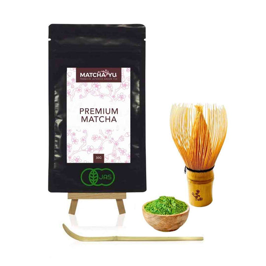 Matcha Yu premium matcha package with a wooden whisk and bowl of green powder on a white background
