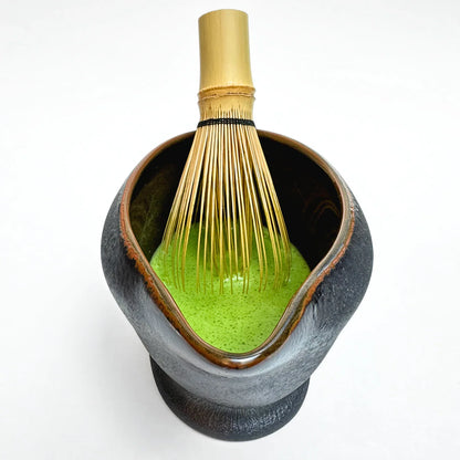 Ceramic Matcha bowl with green powder and a whisk on a white background