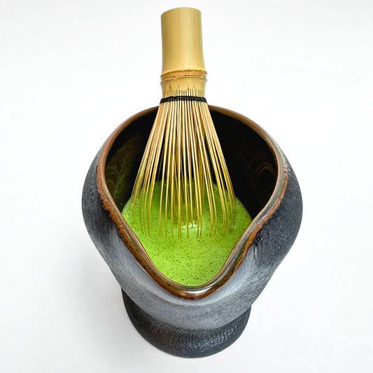 Ceramic Matcha bowl with green powder and a whisk on a white background