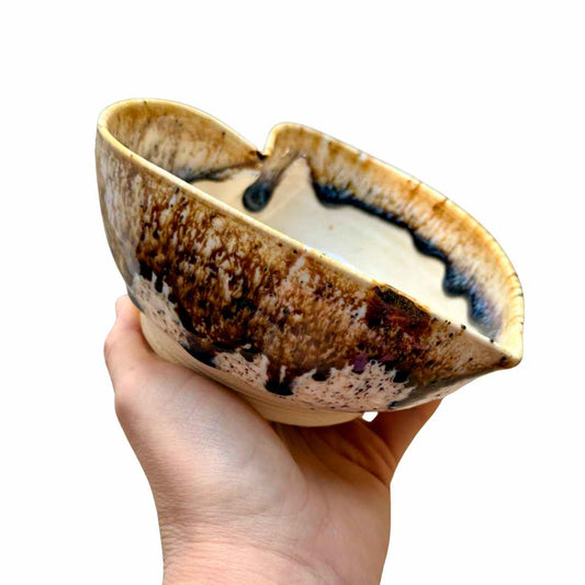 Hand holding a ceramic bowl with a unique glaze pattern on a white background