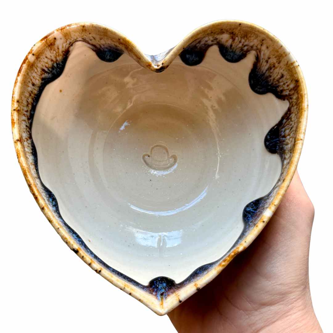 Heart-shaped ceramic bowl with a hand holding it against a white background