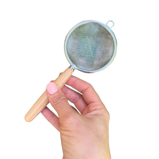 Hand holding a small mesh strainer with wooden handle on a white background