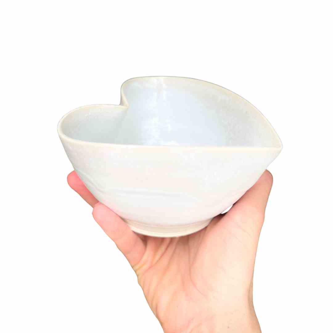 Hand holding a white ceramic bowl with a unique design on a white background