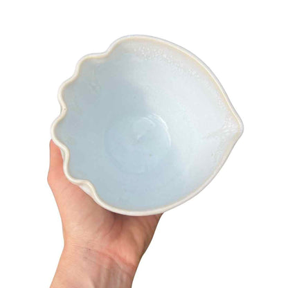 Hand holding a light blue ceramic shell-shaped bowl against a white background